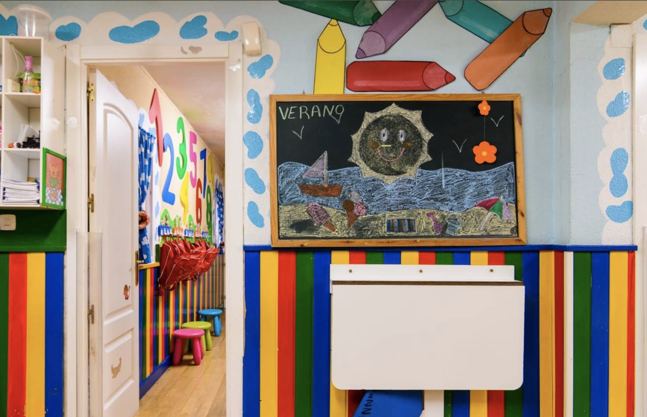 Zona de aula con mesas, juguetes y pared de colores